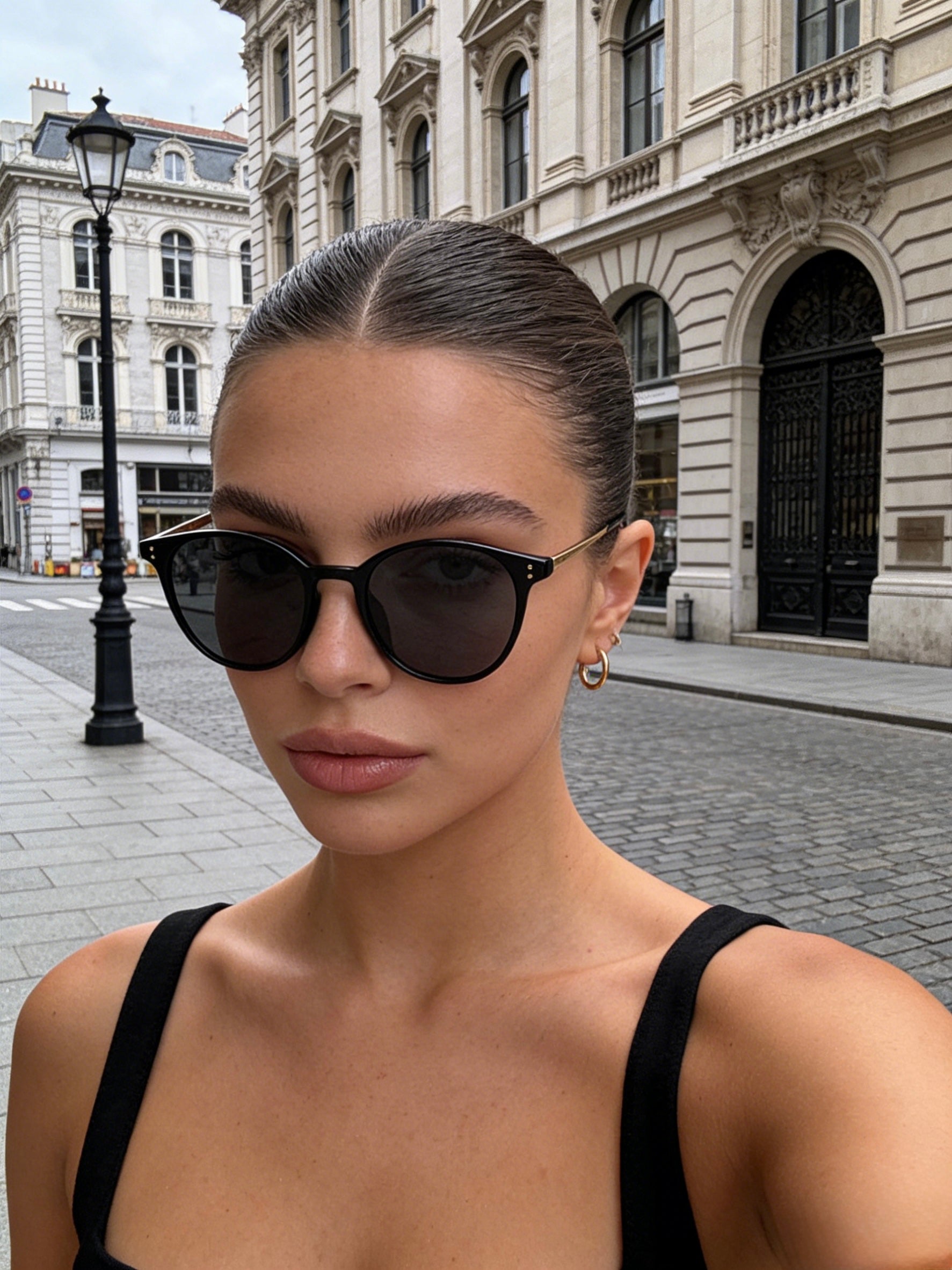 Woman wearing black sunglasses with a city street background. Unisex tortoiseshell round sunglasses with UV protection, polarised lenses, trendy fashion design.