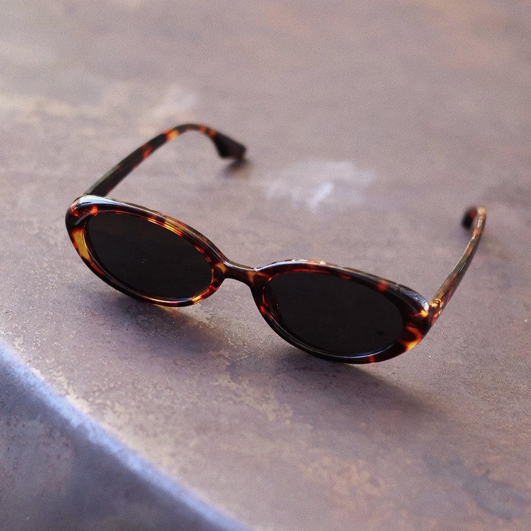 Playful and retro unisex oval sunglasses by By Charley, featuring a distinctive tortoiseshell frame and polarized lenses that offer 100% UV protection and glare reduction for a unique, fashion-forward look.